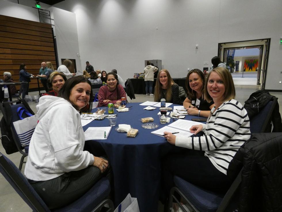 At a table, individuals share smiles, notebooks open on the table from a prior discussion 