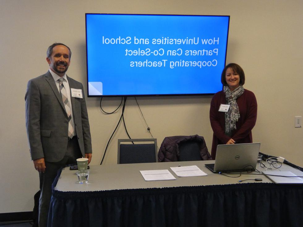 Two individuals stand and smile in front of their presentation