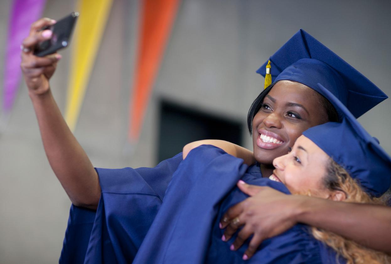 Two graduates take a photo with their phone.